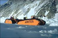 The yellow vehicle, with the word 'ARTKOS' visible on the side, moves across the ice at the base of a mountain